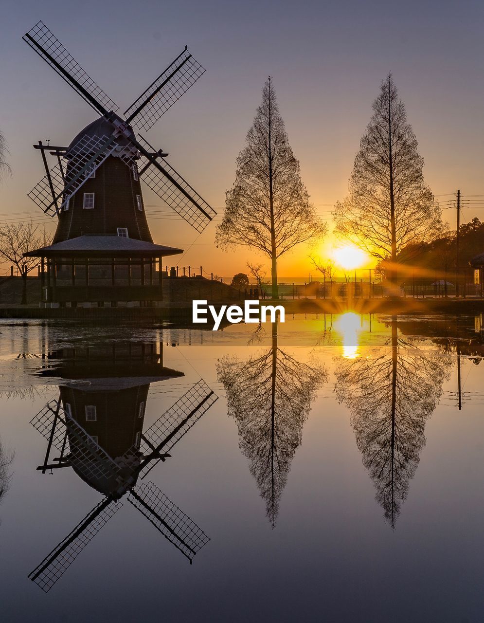 Traditional windmill by lake against sky during sunset