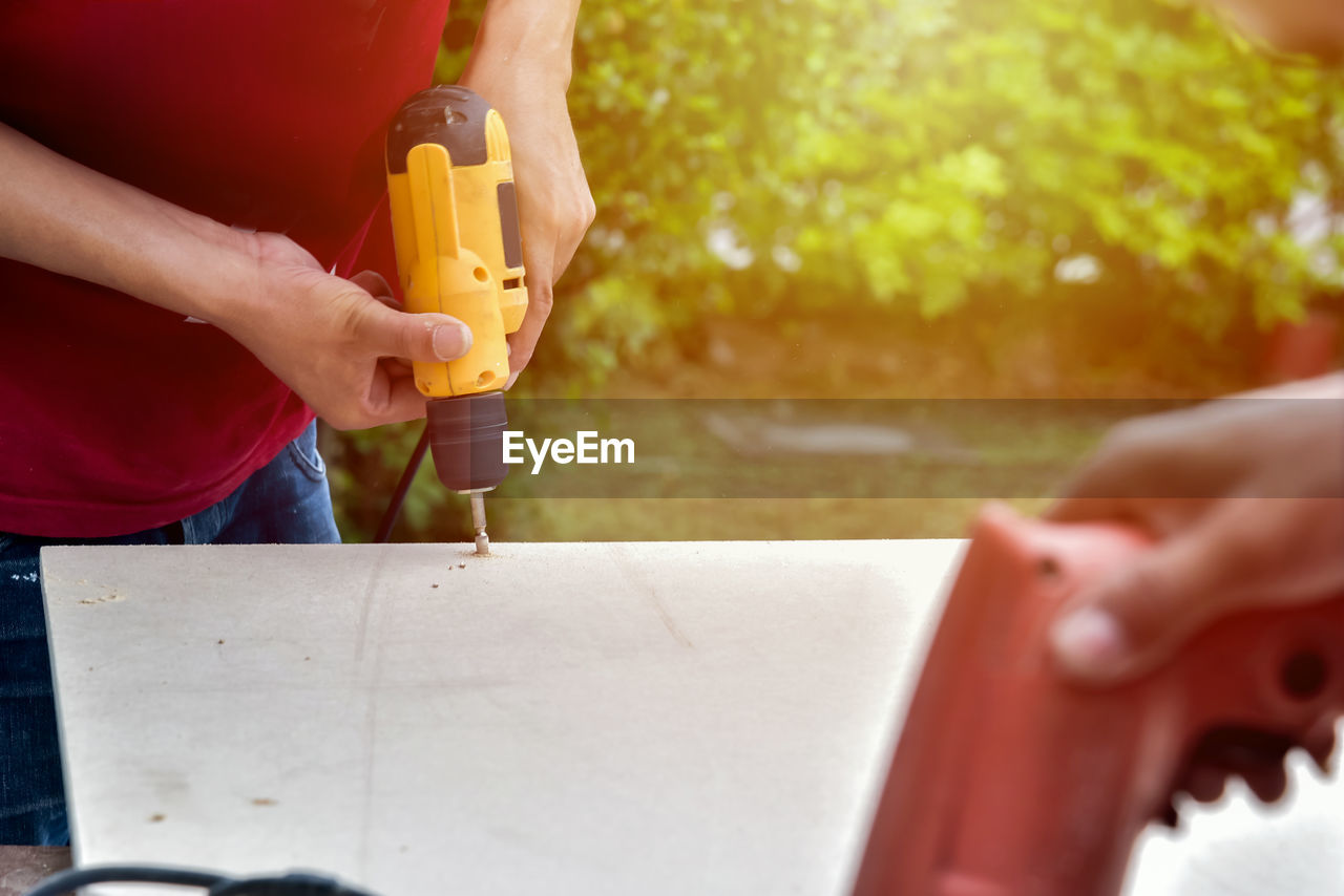 Close-up midsection of man drilling wood outdoors