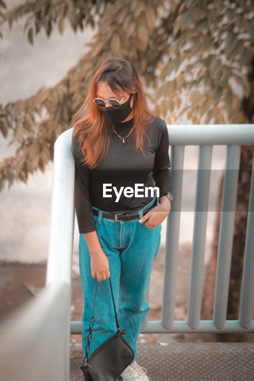 Young woman wearing sunglasses standing on railing