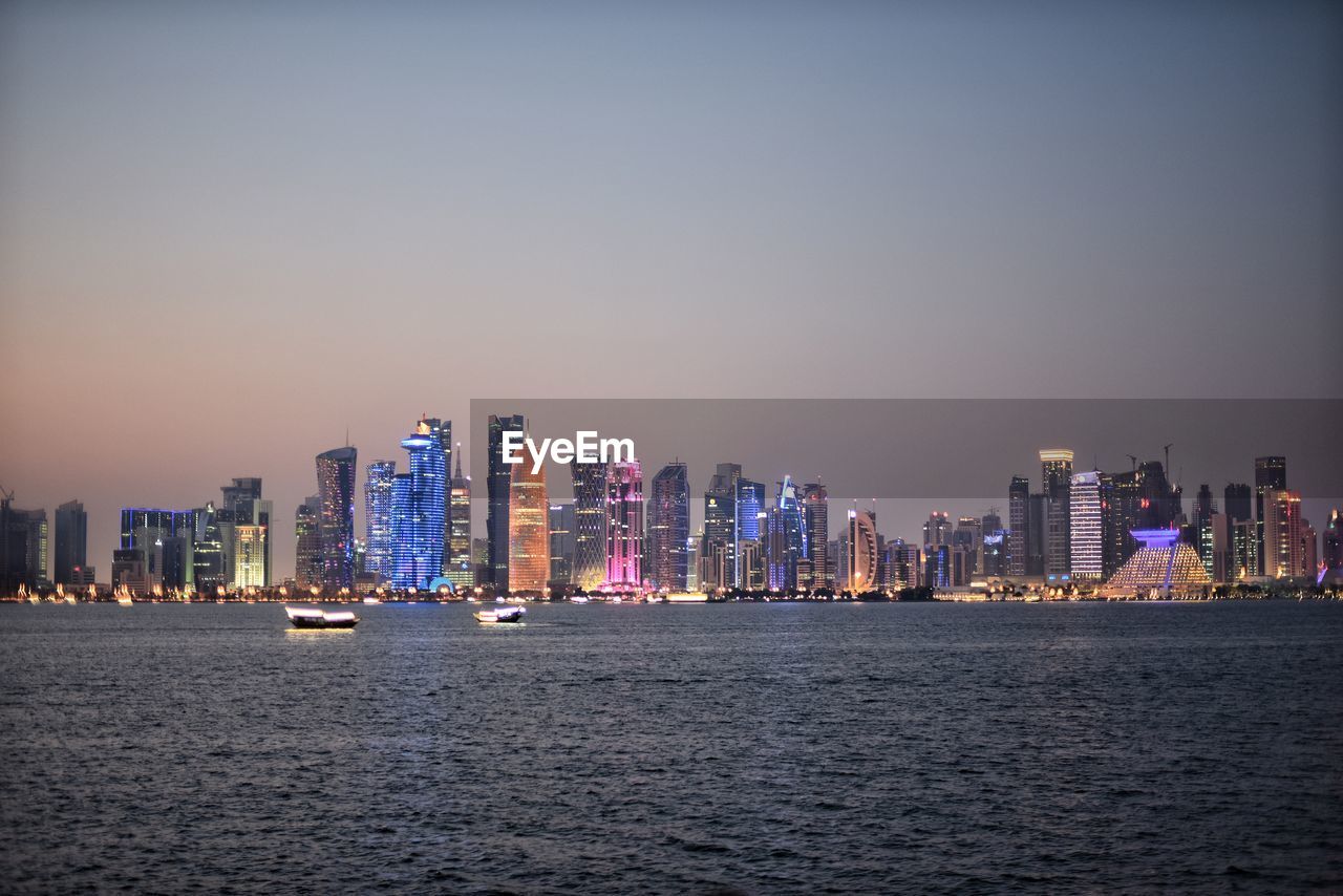 River by illuminated modern buildings against clear sky