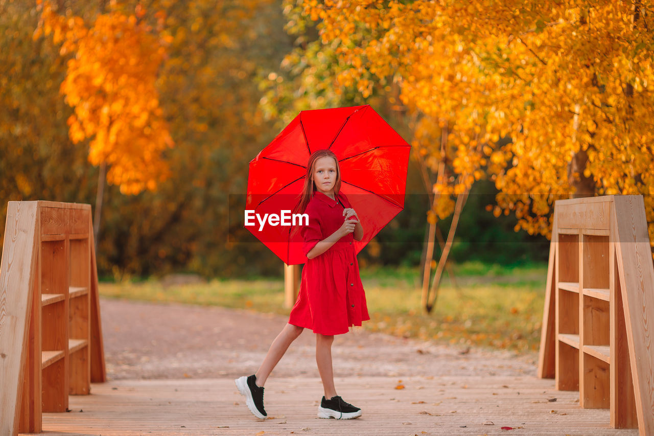 Full length of girl holding red umbrella standing at park