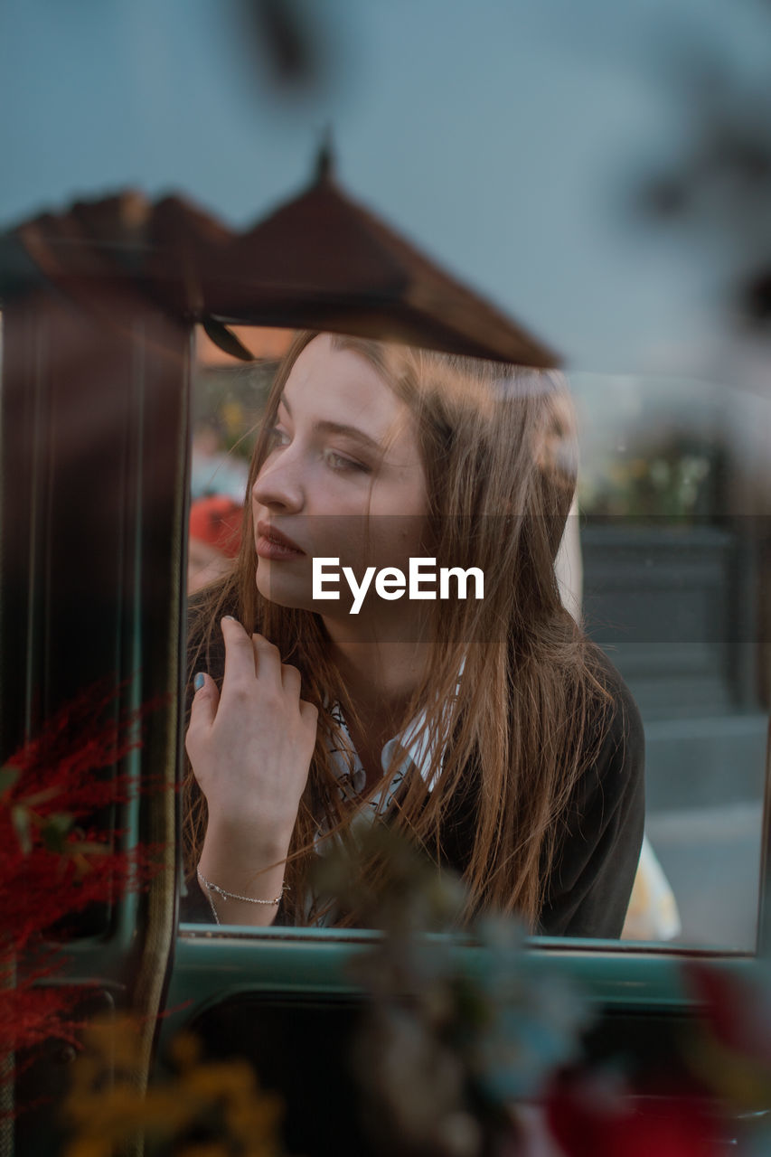 Portrait of young woman looking through window