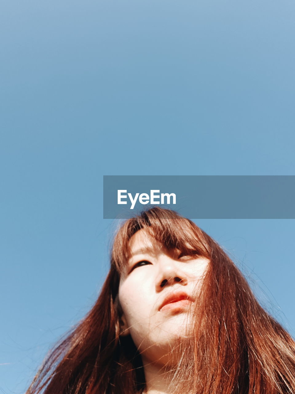 LOW ANGLE PORTRAIT OF WOMAN LOOKING AT AGAINST SKY