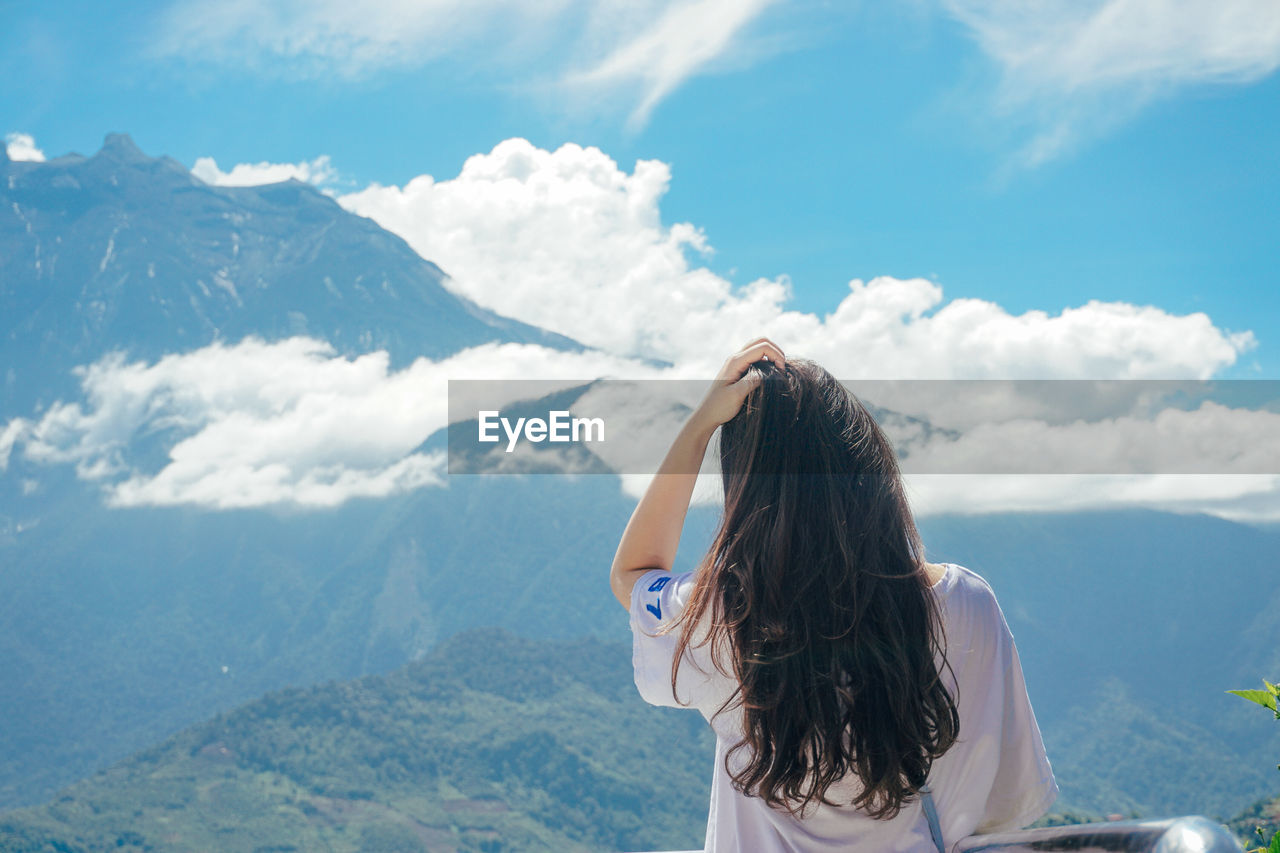 Rear view of woman looking at landscape against sky from mountain peak