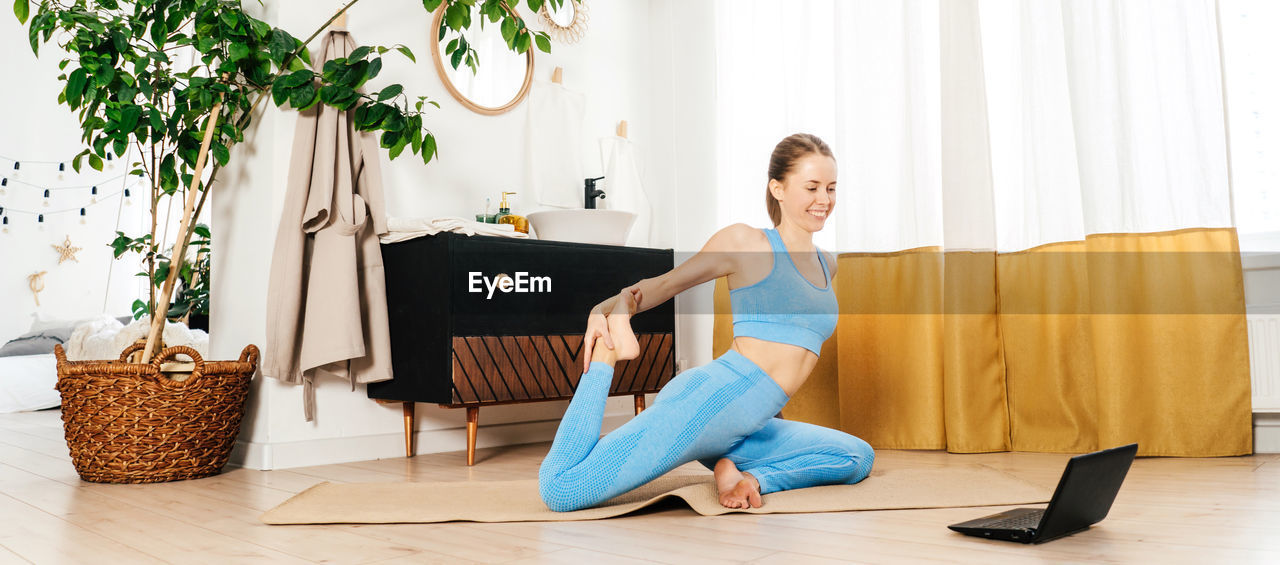 full length of young woman exercising on sofa at home