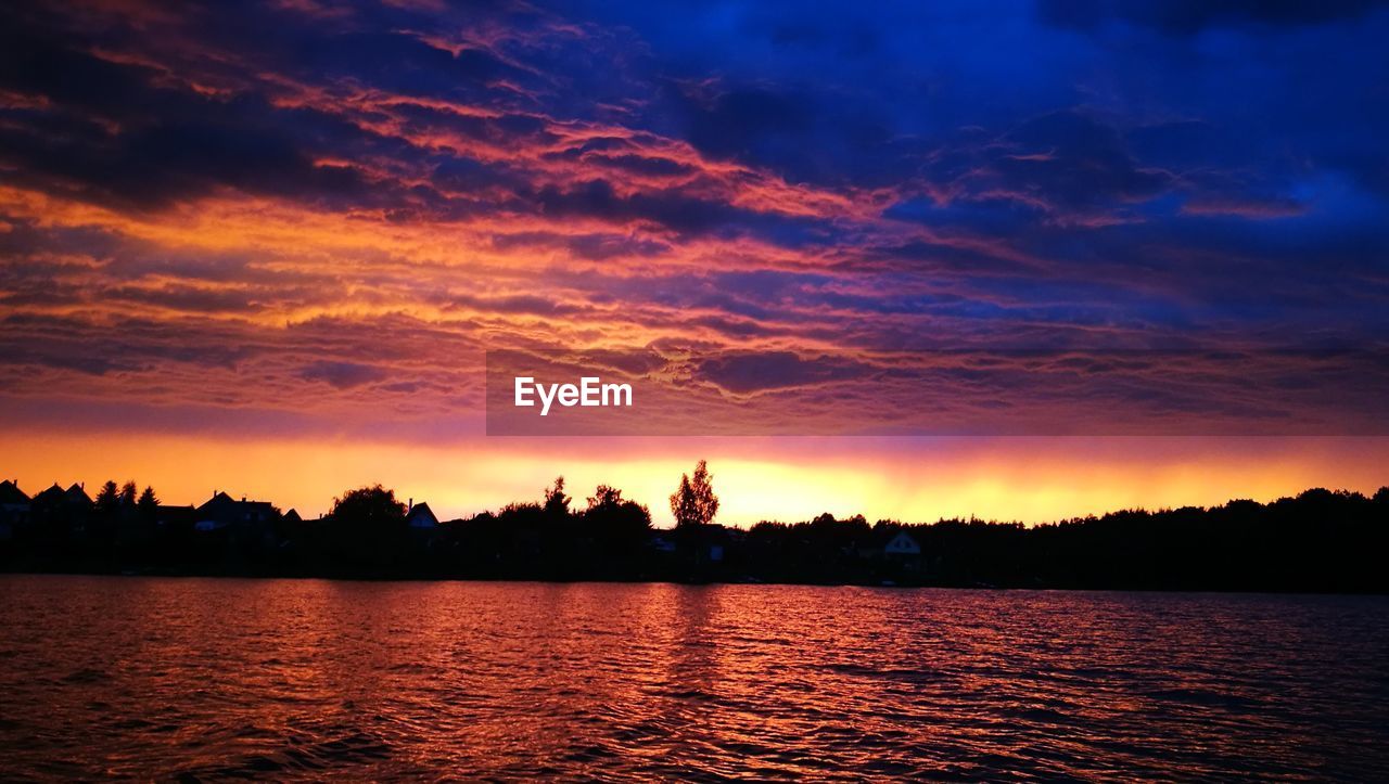 Silhouette trees by lake against sky during sunset