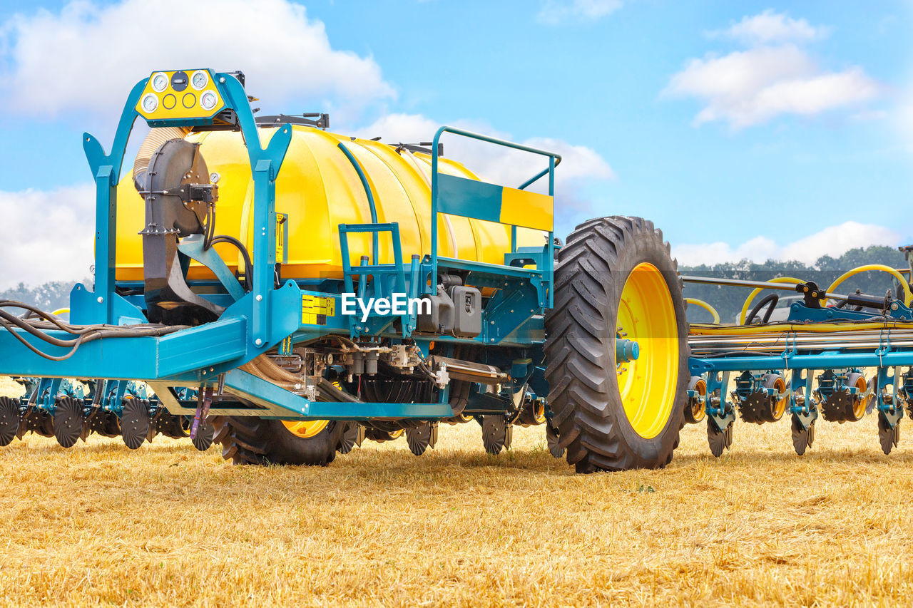 tractor, agriculture, harvester, field, transportation, vehicle, sky, agricultural machinery, machinery, cloud, mode of transportation, nature, landscape, rural scene, land vehicle, land, yellow, farm, day, plant, agricultural equipment, crop, plough, cereal plant, occupation, outdoors, harvesting, blue, construction machinery, combine harvester, industry, equipment, environment, corn, harvest, summer