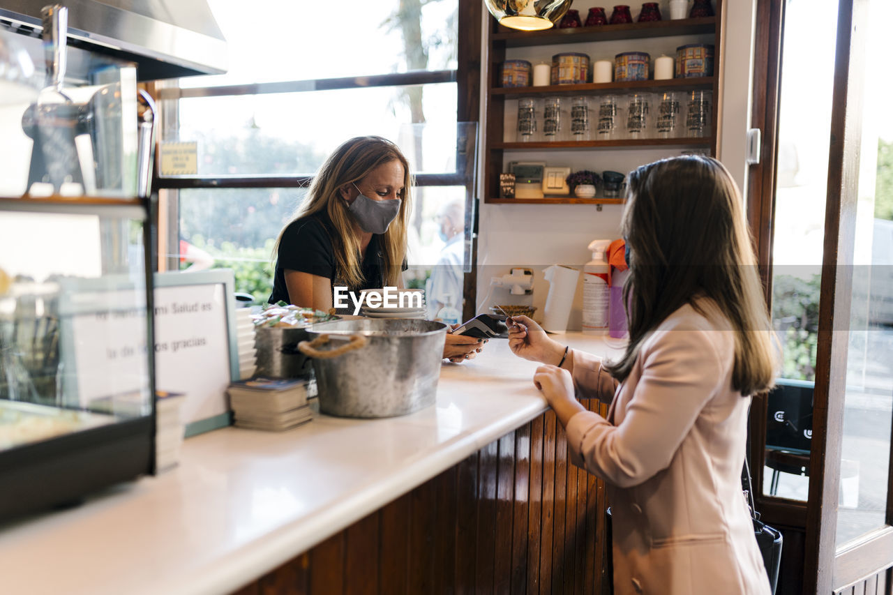 Young businesswoman paying through credit card at counter in coffee shop during covid-19