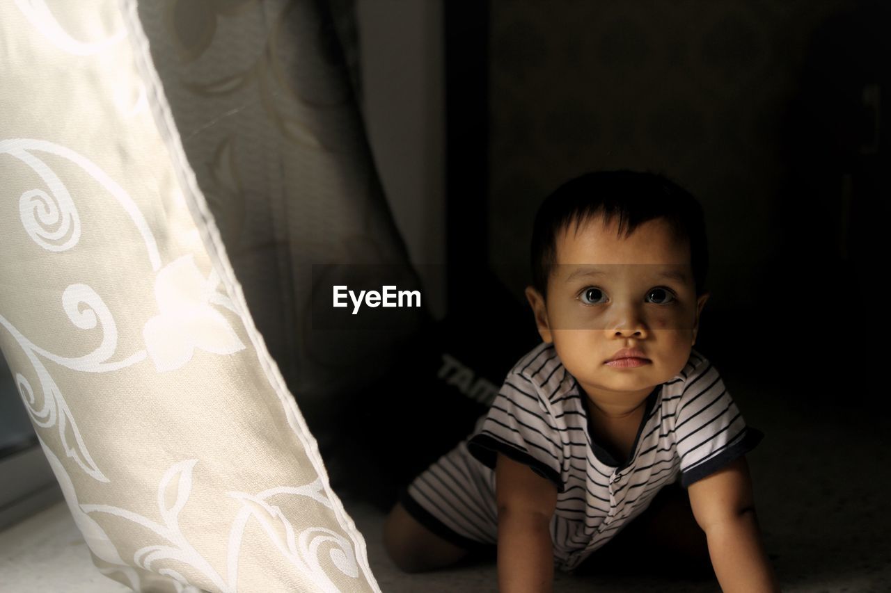 Cute baby boy crawling by curtain at home