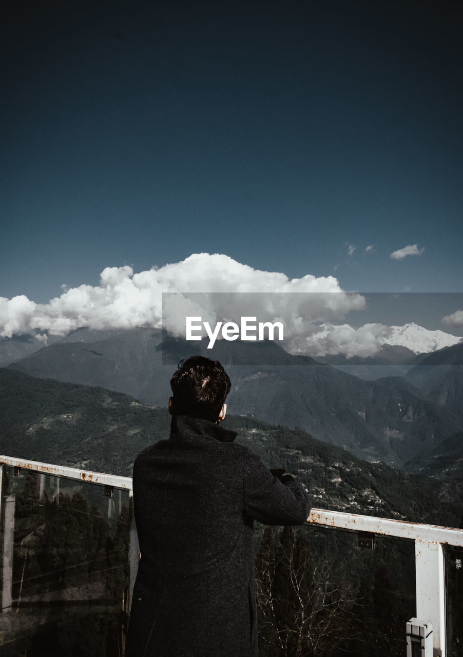 Rear view of man standing on mountain against sky