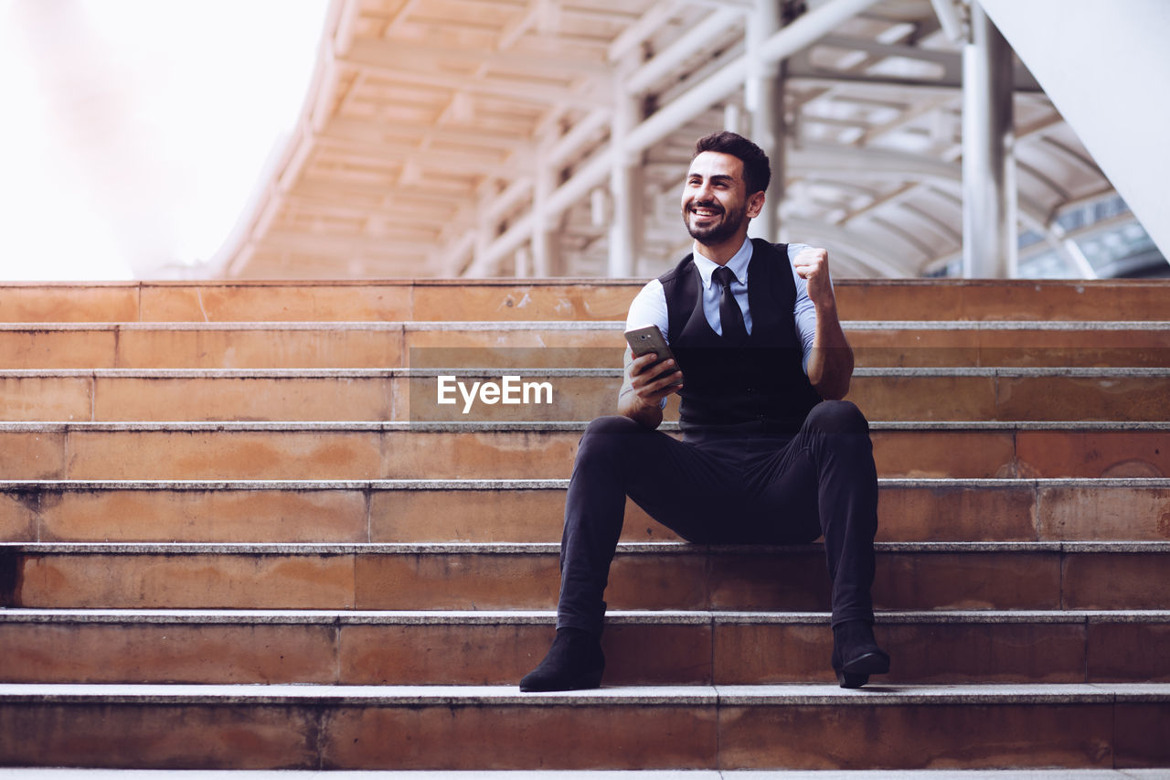 Full length of businessman using mobile phone while sitting on staircase