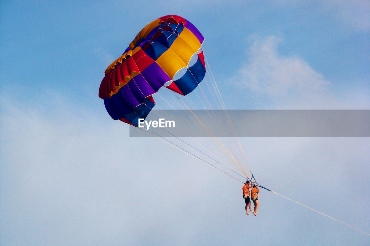 Low angle view of couple parasailing against sky