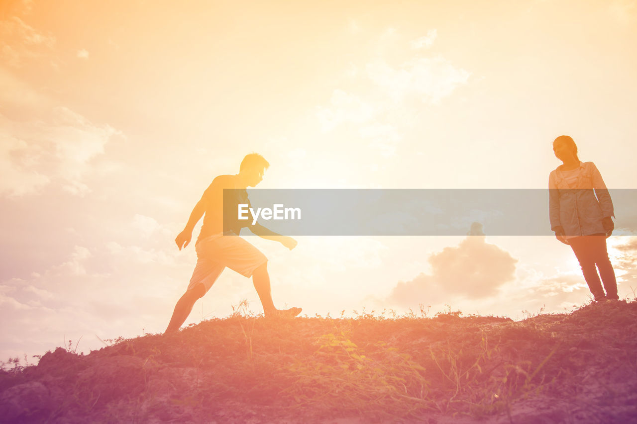 MAN AND WOMAN STANDING ON FIELD AGAINST SKY