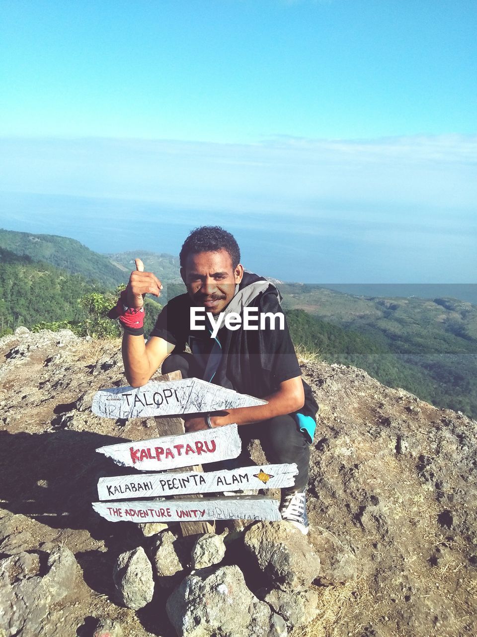 High angle view of man crouching on cliff against sky