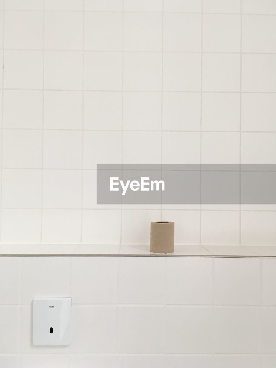 Close-up of brown toilet paper against white tiled wall in bathroom