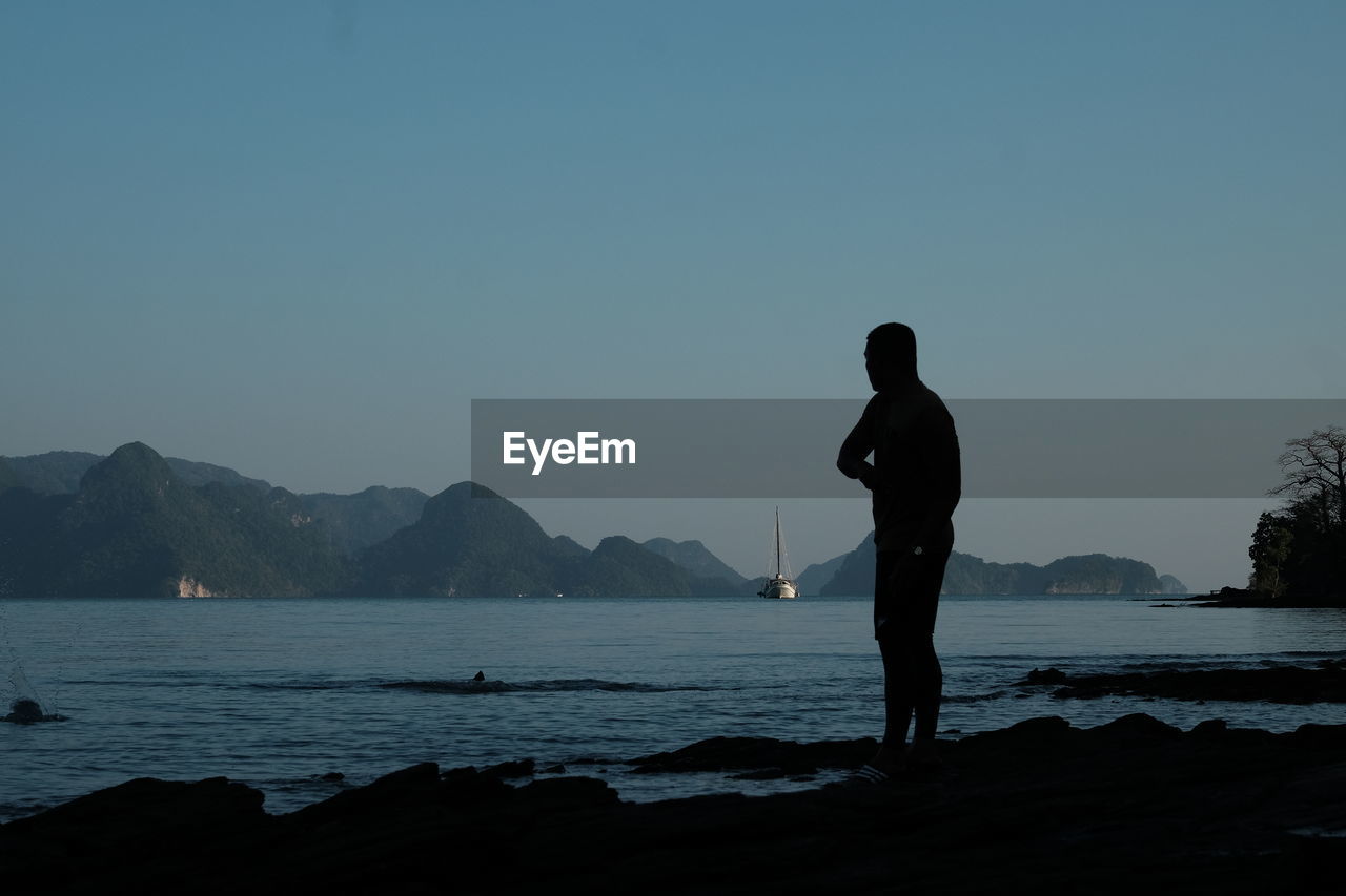 Silhouette man standing by lake against clear sky