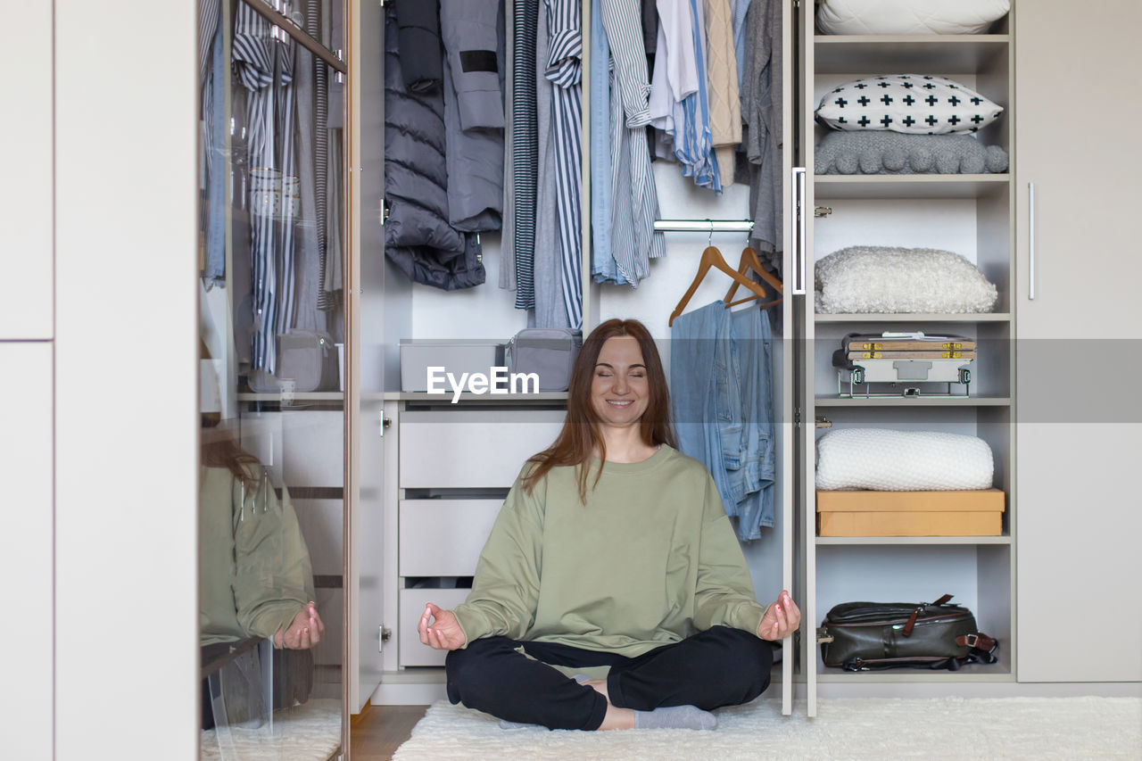 Cheerful woman meditating by closet at home