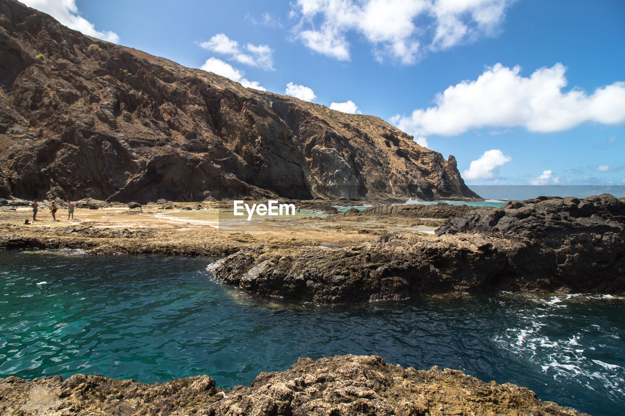 Scenic view of rocks by sea against sky