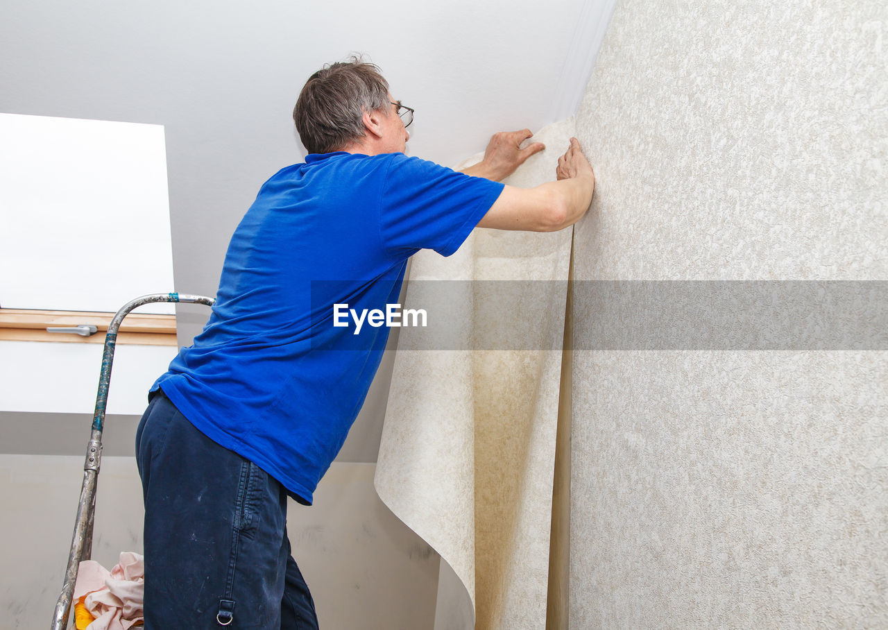 Side view of painter putting wallpaper on wall at construction site