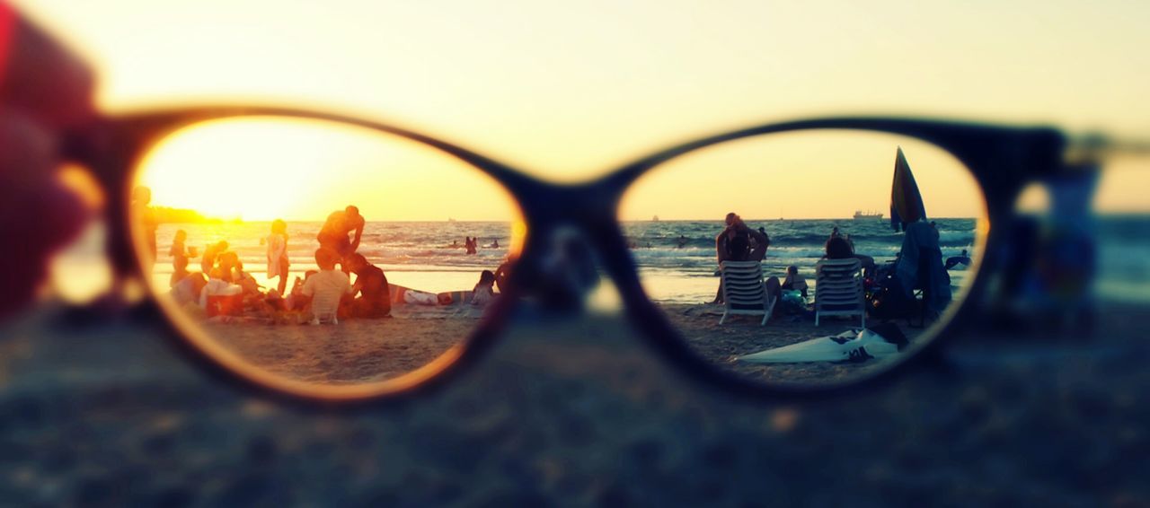 People enjoying vacation on beach seen through eyeglasses