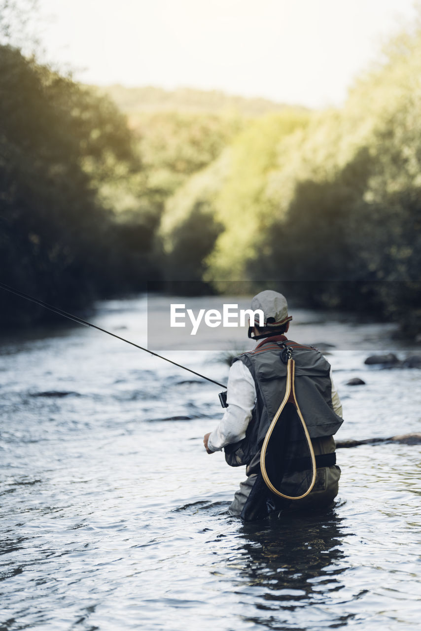 REAR VIEW OF MAN FISHING AT LAKE