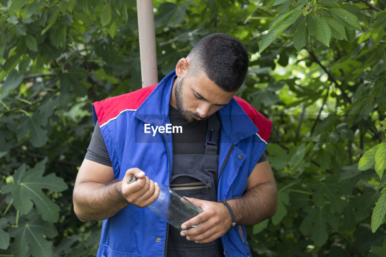 YOUNG MAN LOOKING AWAY AGAINST PLANTS