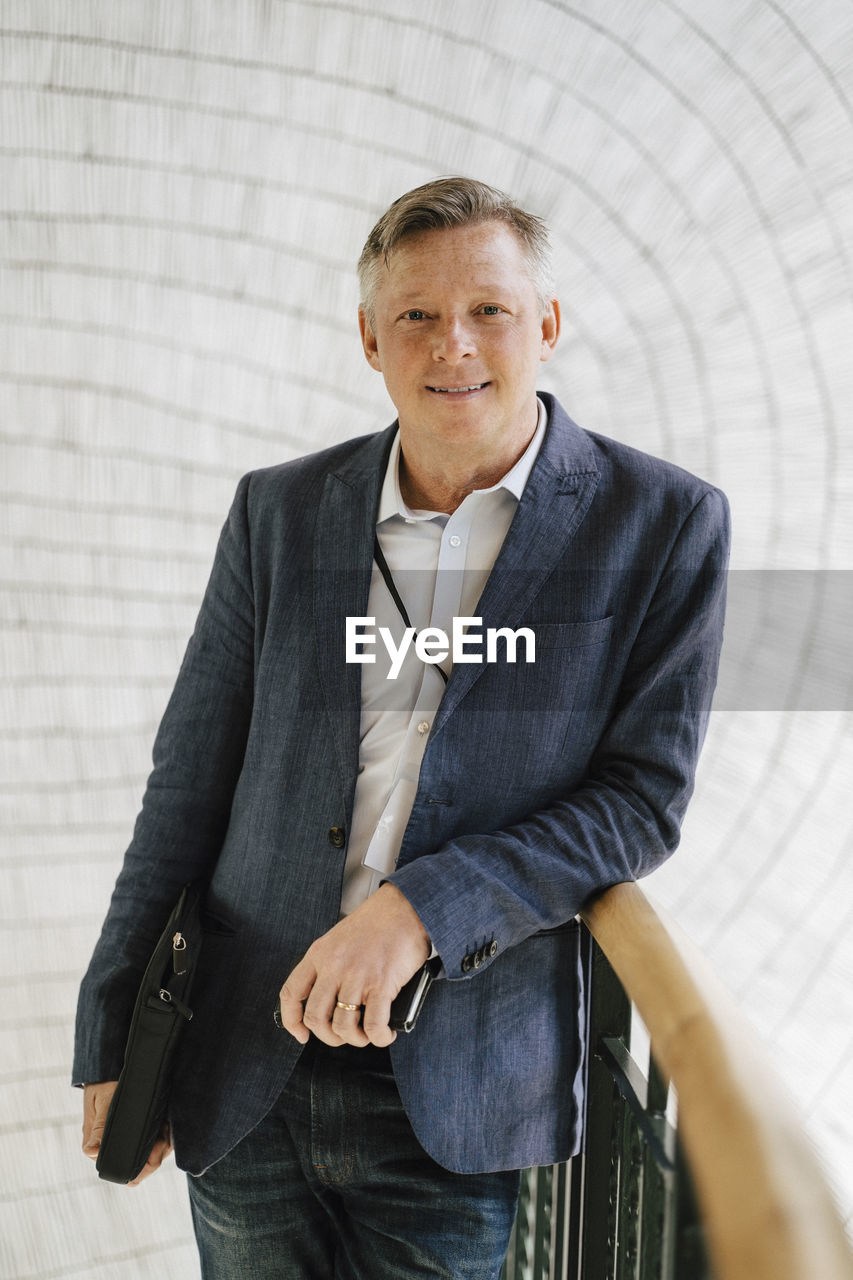 Portrait of mature businessman standing leaning on railing at convention center