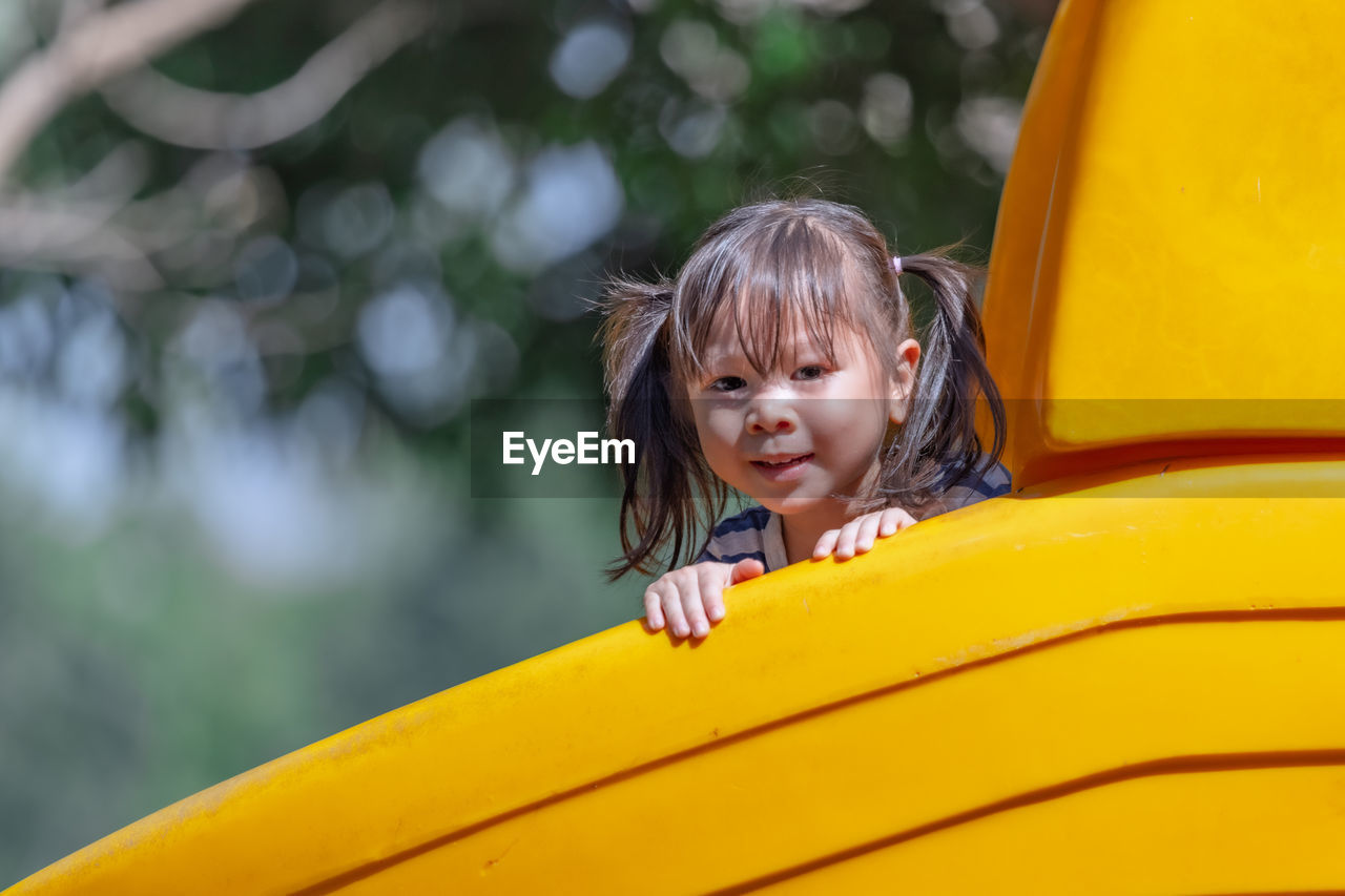 Close-up portrait of girl peeking behind play equipment