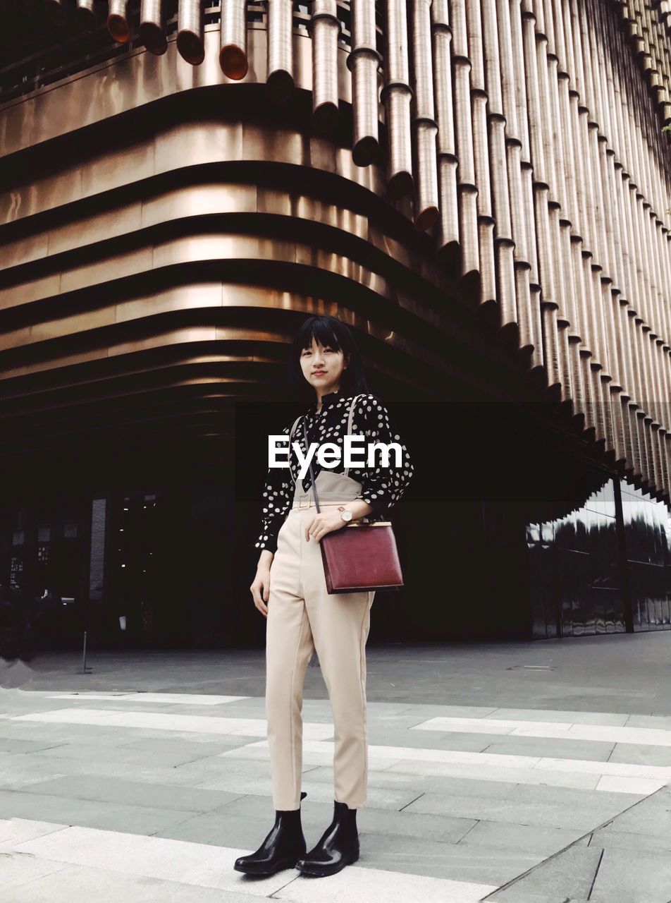 Full length portrait of woman standing on footpath against building