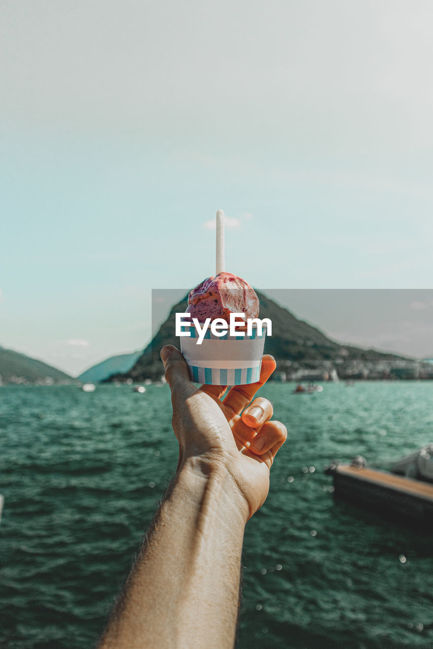 Midsection of person holding ice cream against sea