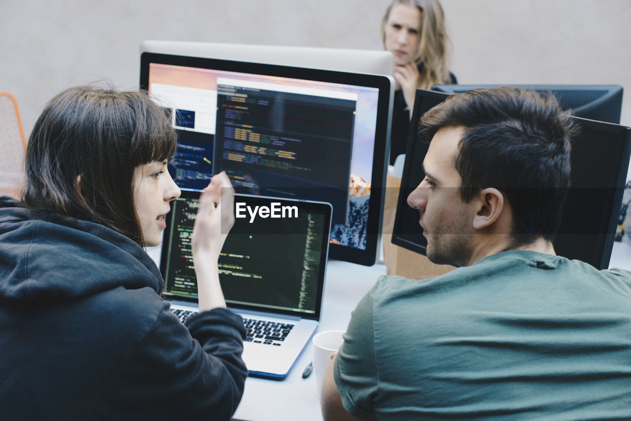 Rear view of computer programmers discussing at office desk