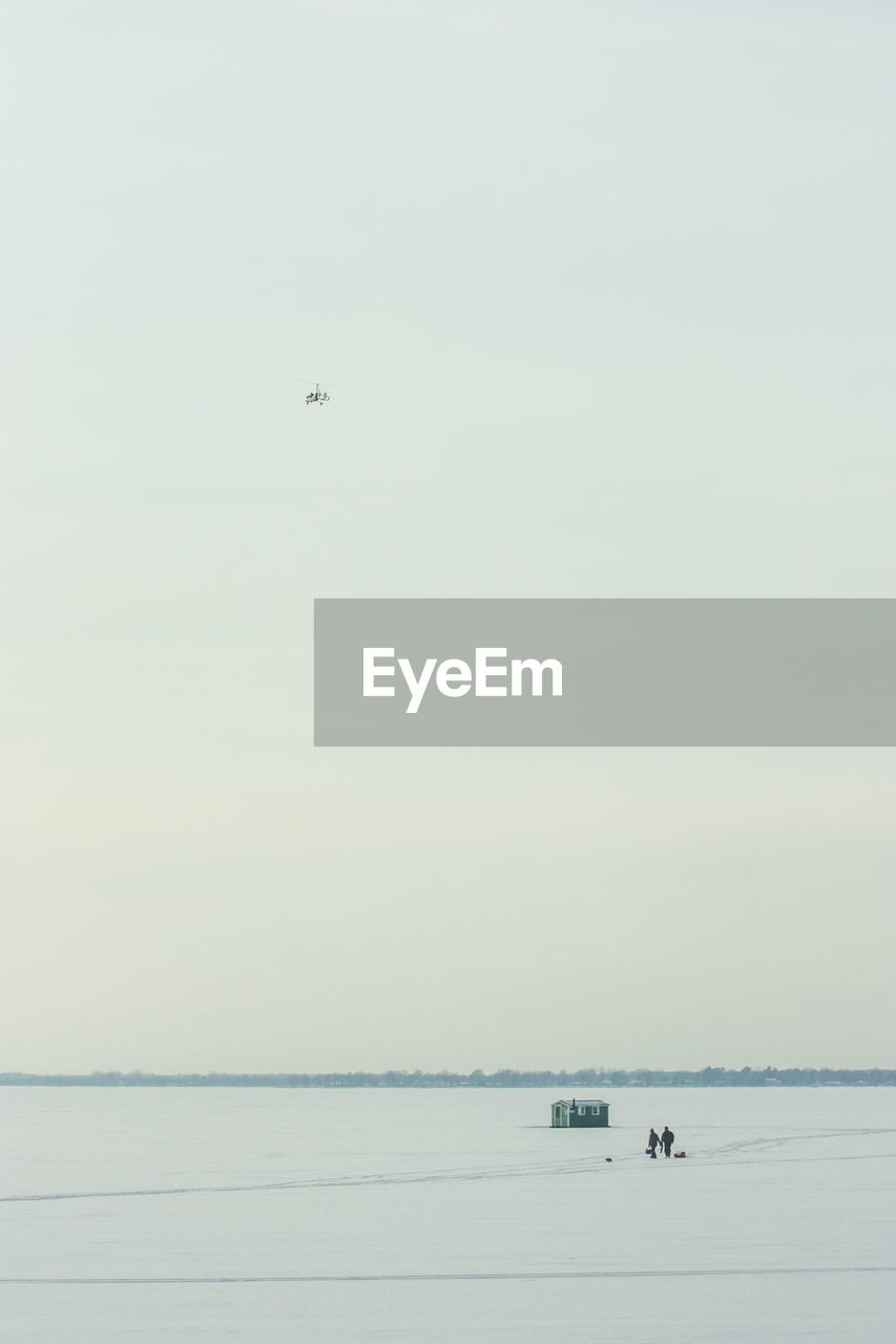 AIRPLANE FLYING OVER SEA AGAINST CLEAR SKY