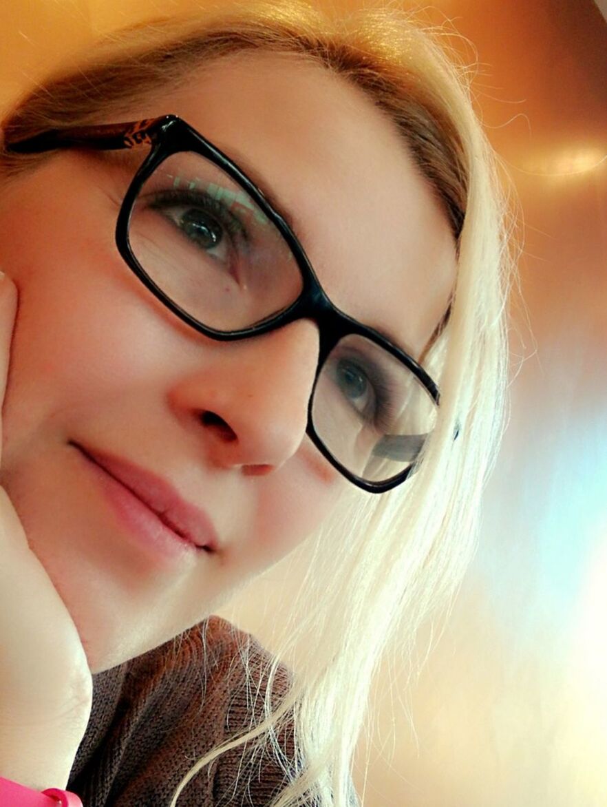 Close-up of smiling thoughtful woman wearing eyeglasses against wall