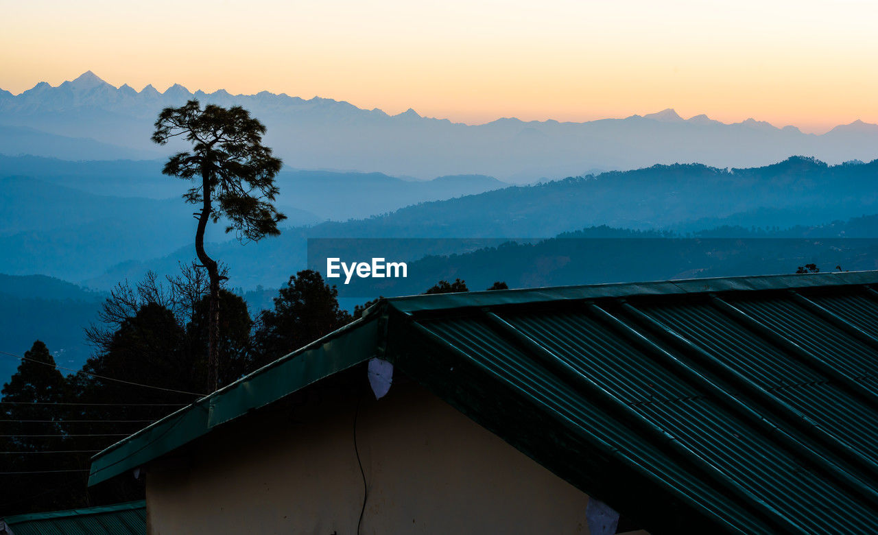 mountain, sky, architecture, mountain range, environment, scenics - nature, nature, landscape, built structure, morning, dawn, beauty in nature, sunrise, tree, sunlight, house, roof, building exterior, building, horizon, plant, sun, no people, cloud, travel destinations, land, tranquility, twilight, mountain peak, outdoors, travel, fog, tranquil scene, rural scene, residential district, forest, silhouette, city