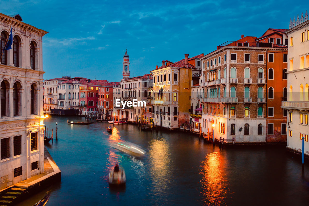 Venice's grand canal at sunset with illuminated historic buildings and light trails of tourist boats