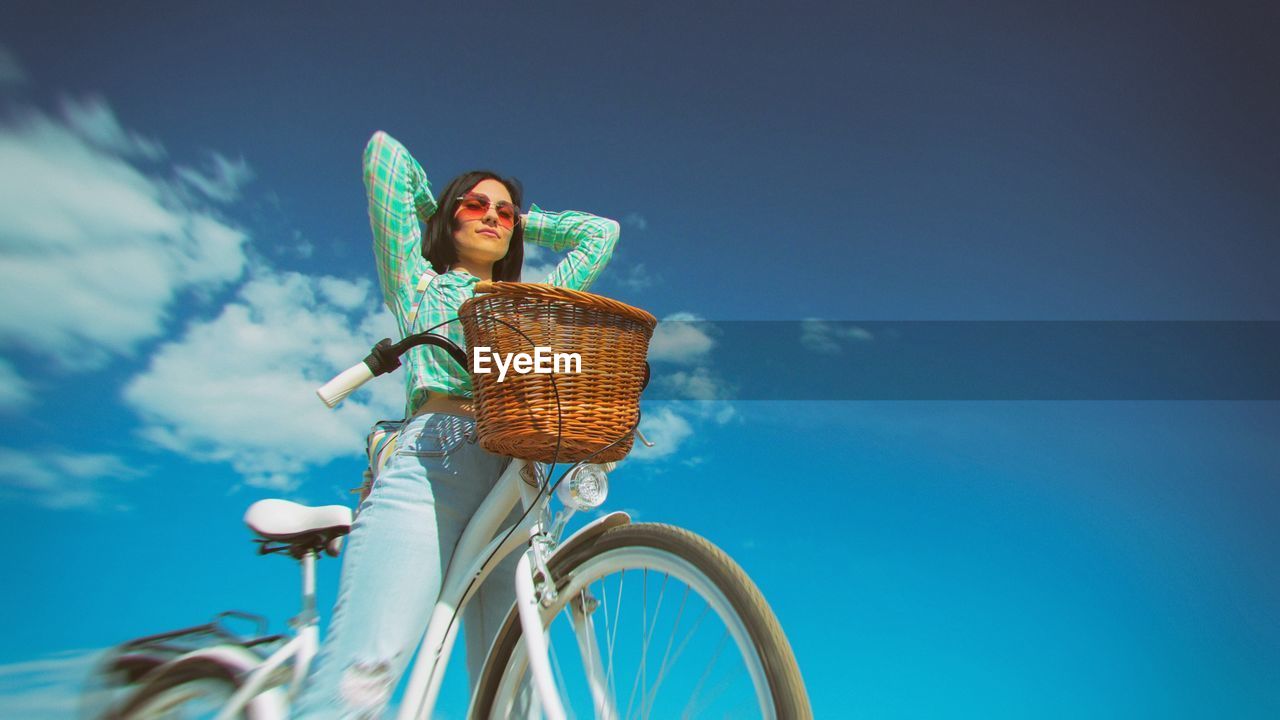 Low angle view of young woman with bicycle against sky