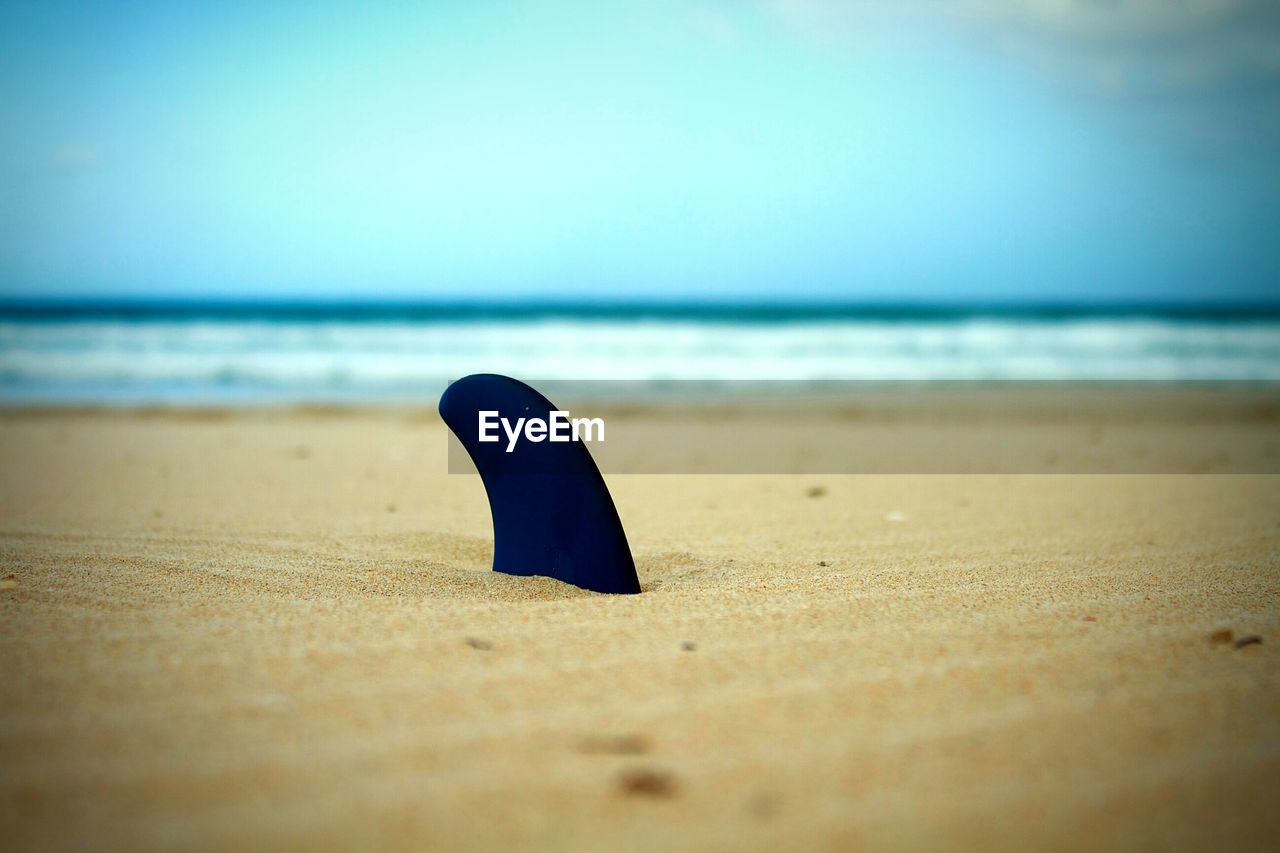 Surface level shot of shark fin in sand on sea shore against sky