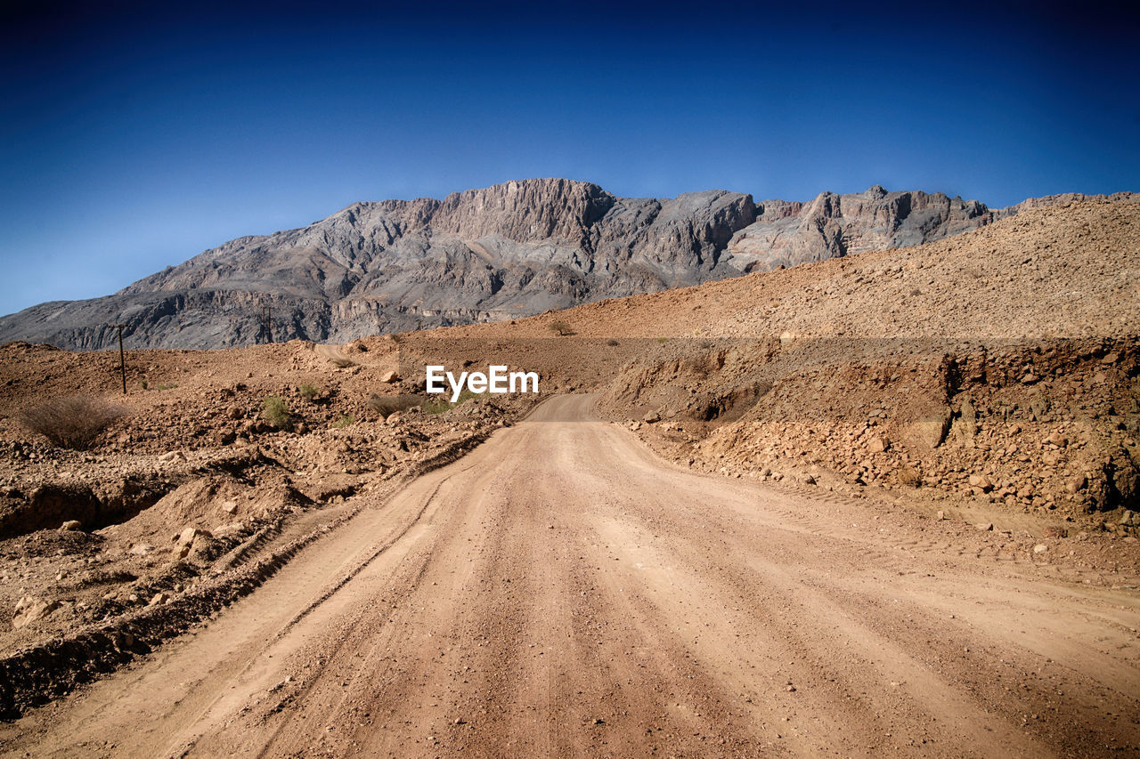 Dirt road in desert against clear sky