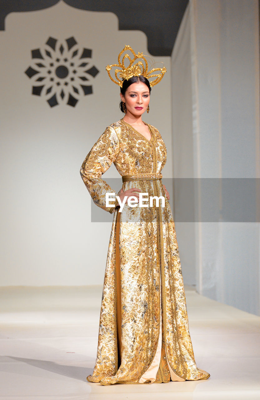 PORTRAIT OF A YOUNG WOMAN STANDING IN FRONT OF TRADITIONAL CLOTHING