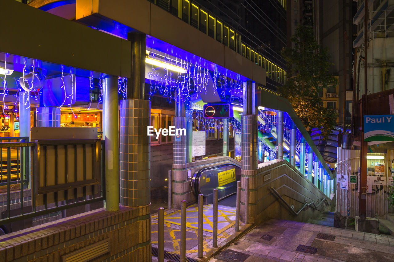 ILLUMINATED STREET LIGHT ON BRIDGE AGAINST BUILDINGS IN CITY