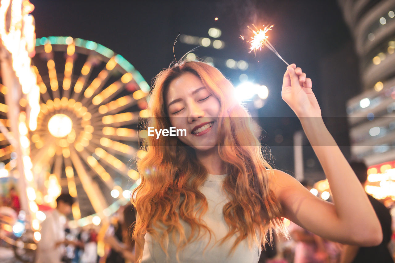 Smiling woman with sparkler standing in illuminated city at night