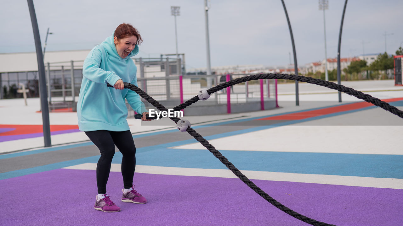 Full length of woman exercising battle rope outside