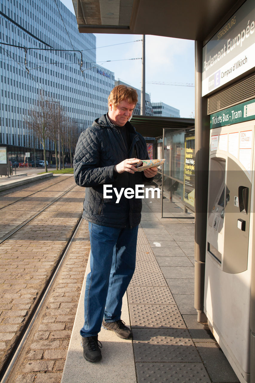 FULL LENGTH OF MAN USING MOBILE PHONE WHILE STANDING ON OFFICE