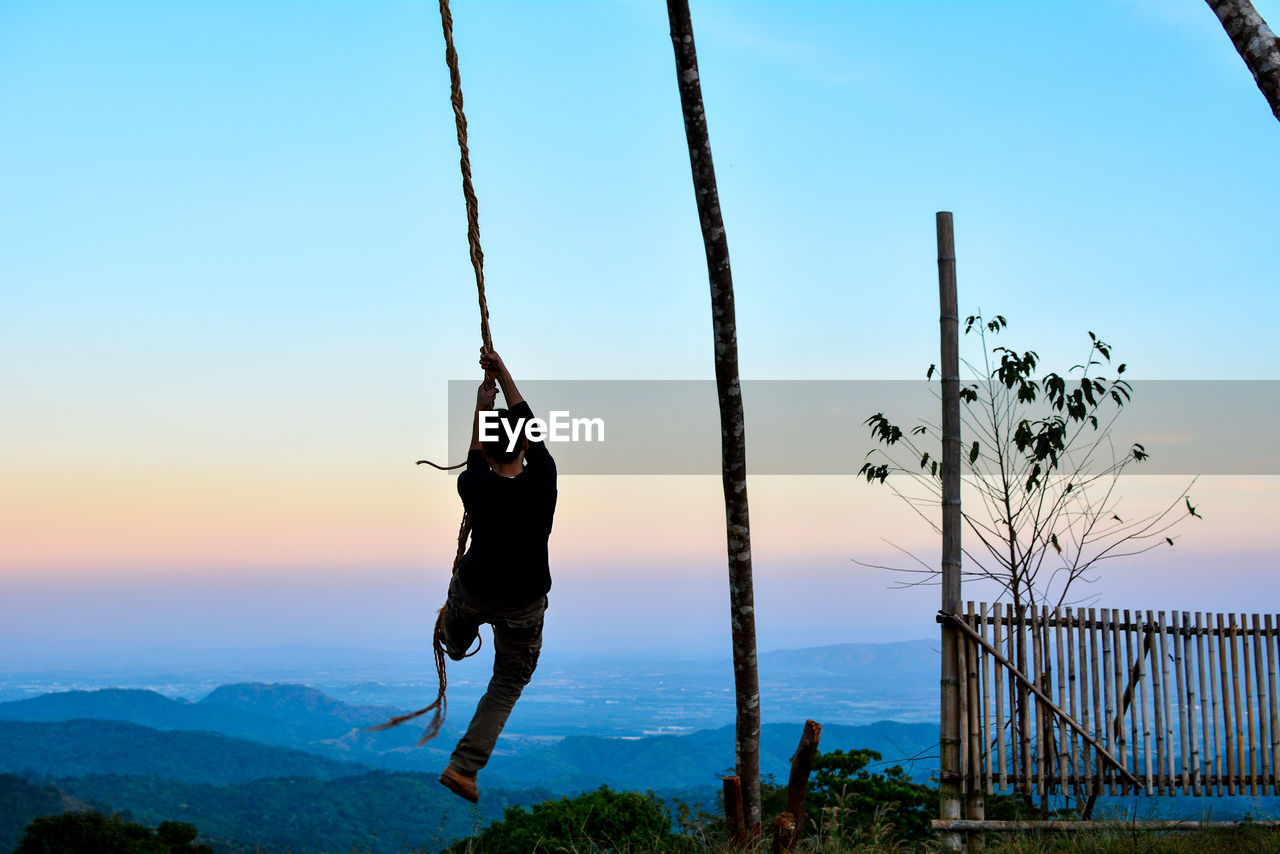 Rear view of man playing on rope against sky
