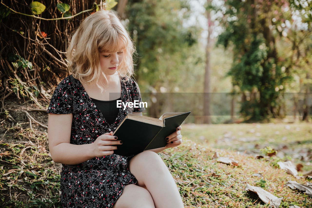 Young woman reading book while sitting on field