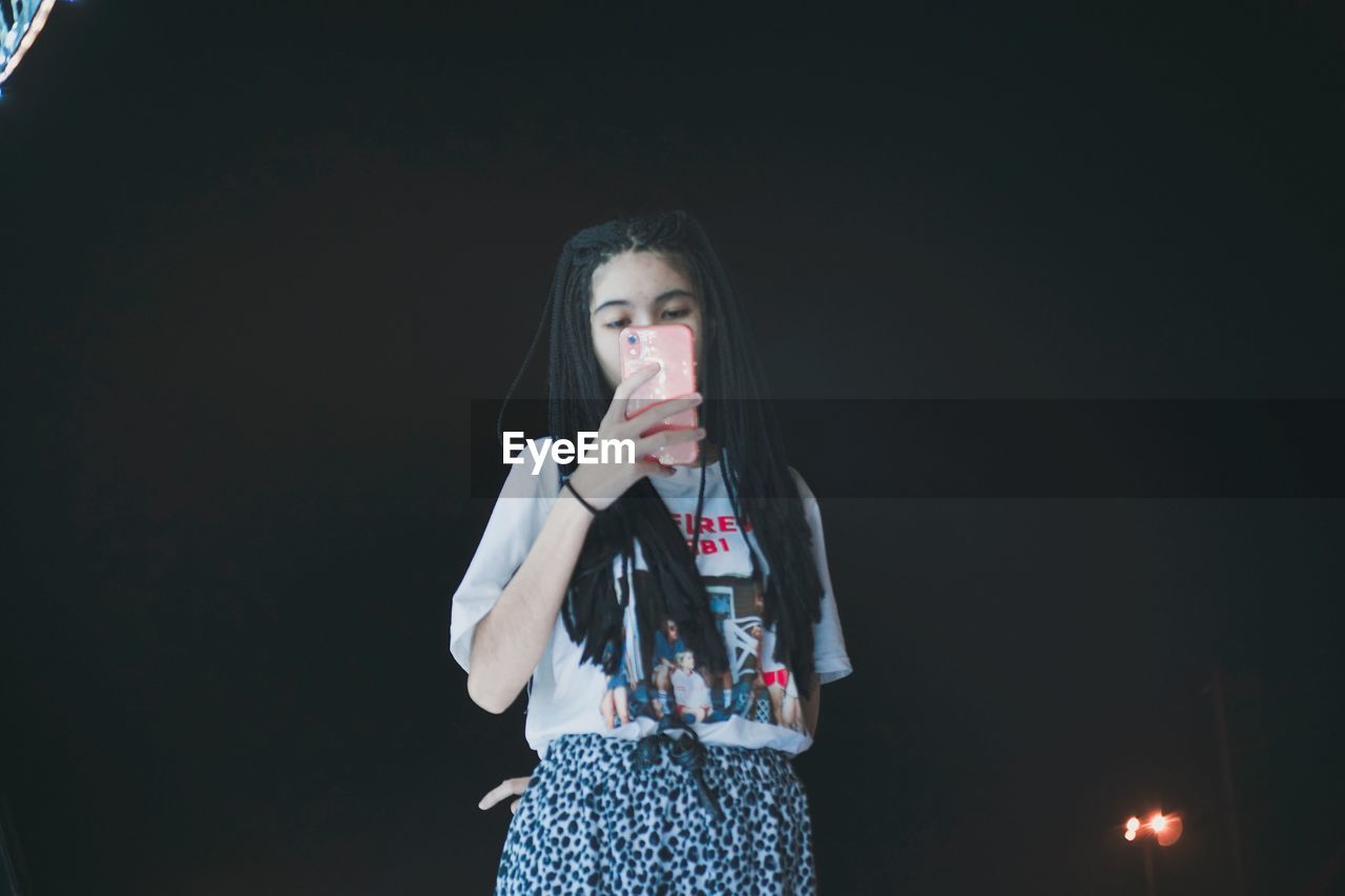 Low angle view of young woman photographing while standing against sky during night