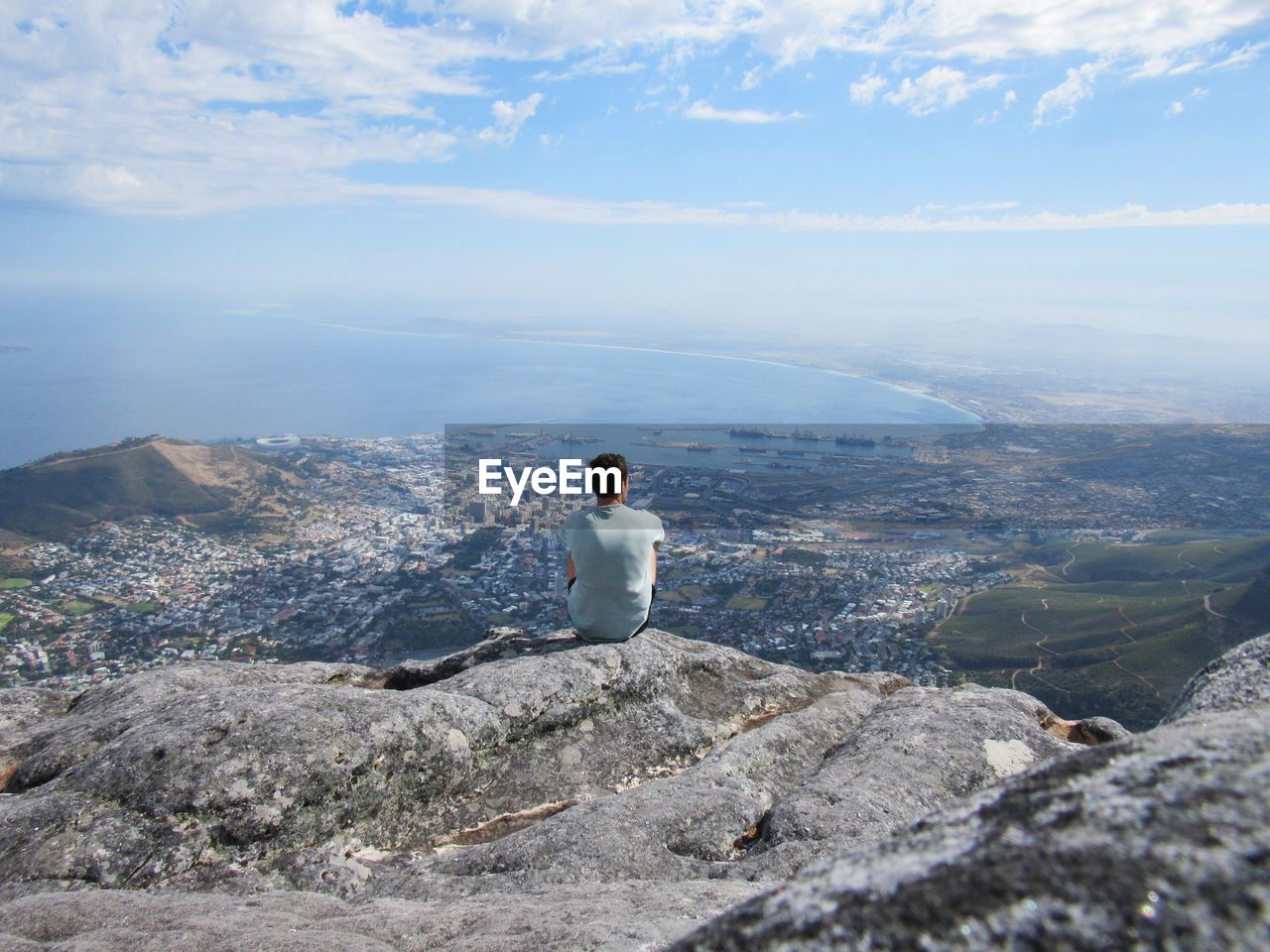 Man sitting on cliff against sky