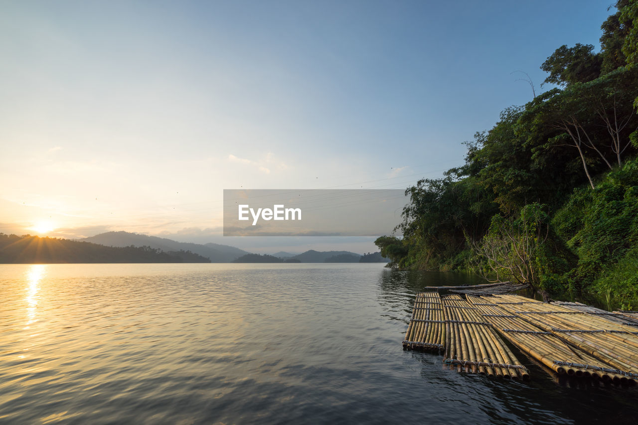 Wooden rafts moored on lake by trees against cloudy sky