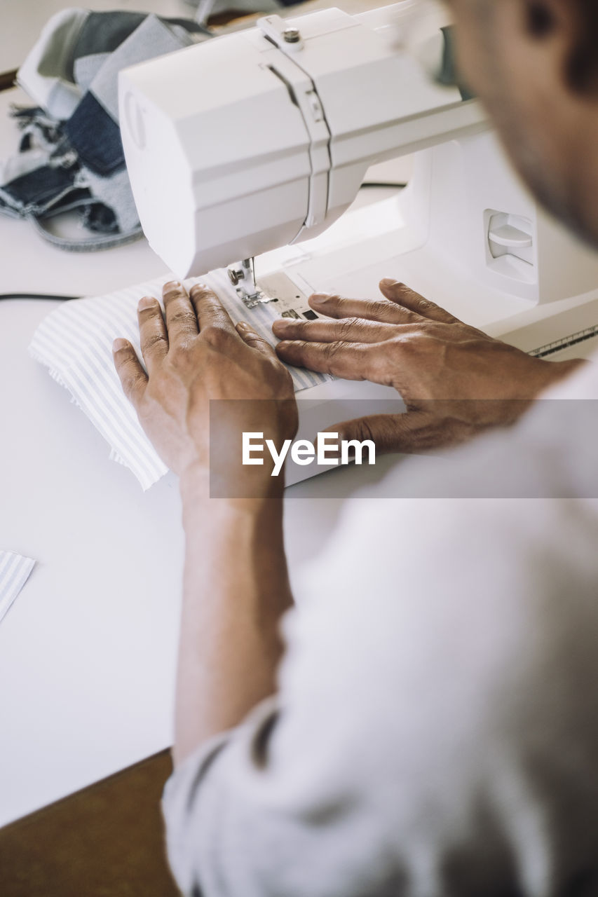 Male fashion designer sewing cloth using sewing machine while working at workshop