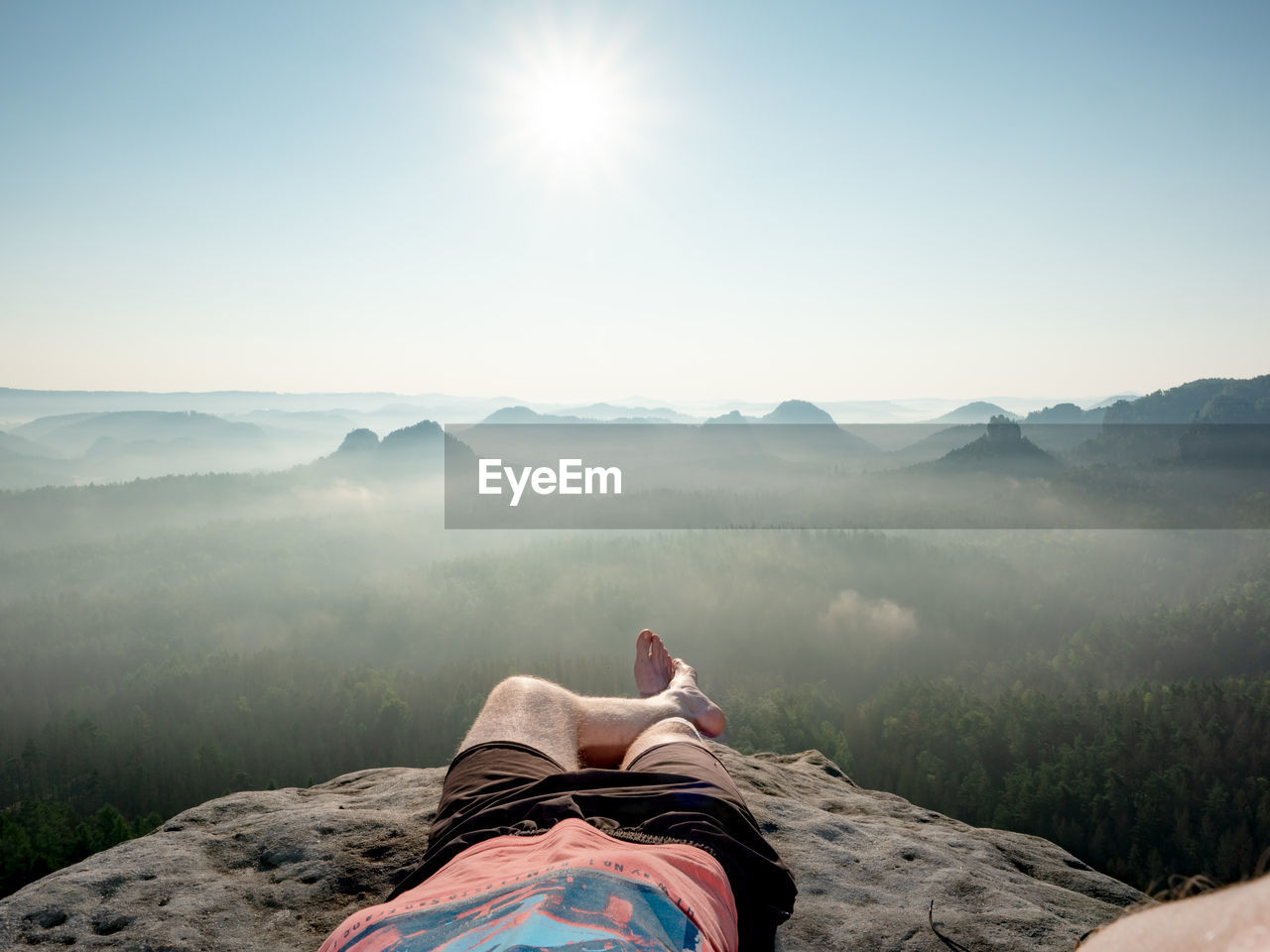 Hiker with bare feet lie on  edge of rock and relax. view over resting male body into morning land